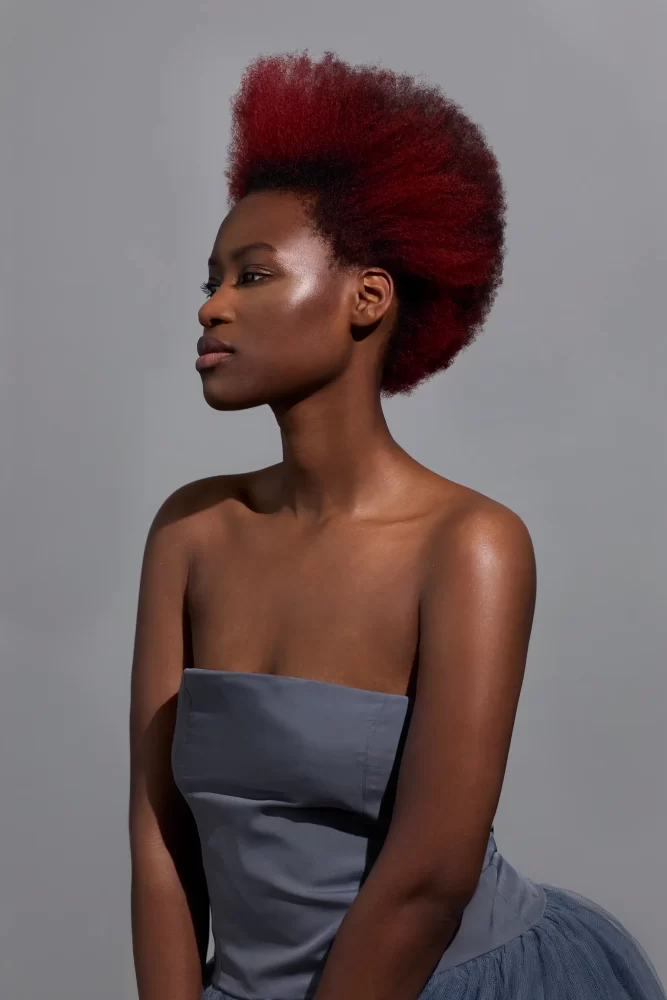 Modelo con corte afro moderno en color rojo vibrante, parte de la colección Iconic de Sassoon Academy.