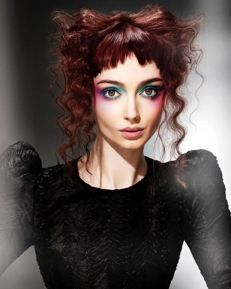 Modelo con cabello rizado rojizo profundo, peinado en volumen y maquillaje vibrante, colección Freedom por Kerry Mather.