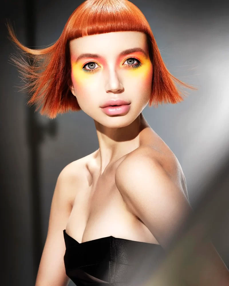 Modelo con corte bob corto en tono cobre brillante, maquillaje naranja intenso, colección Freedom por Kerry Mather.