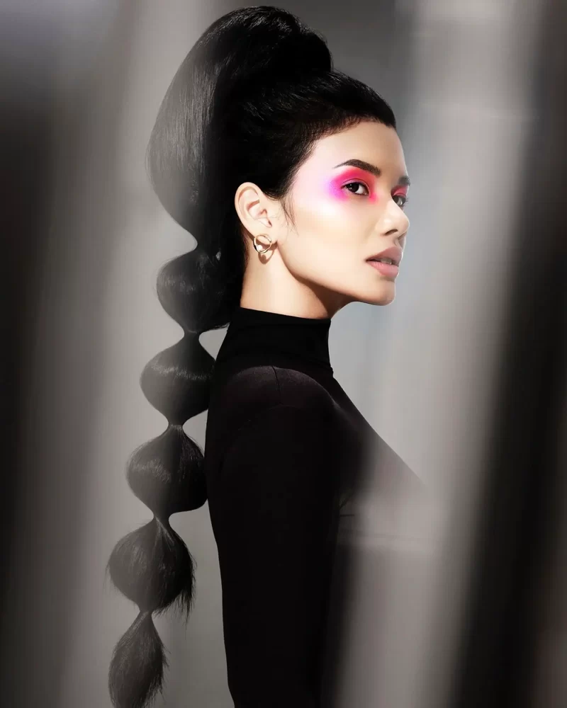 Modelo con coleta alta estructurada en cabello negro azabache y maquillaje rosa vibrante, colección Freedom por Kerry Mather.