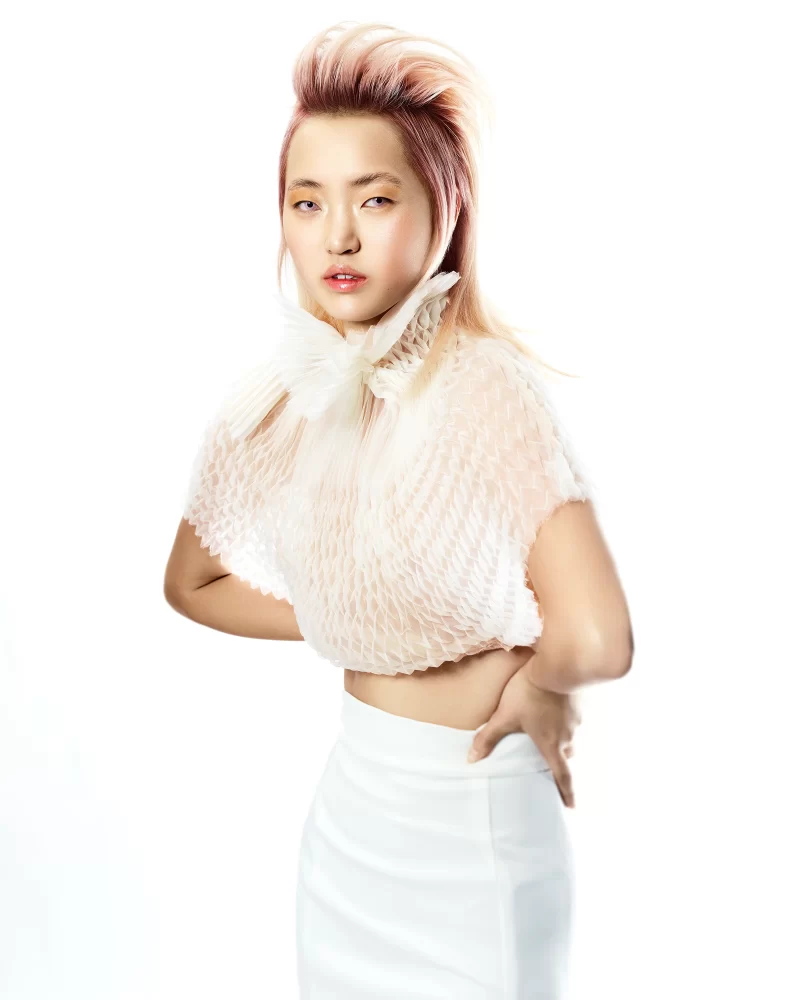 Modelo con peinado voluminoso en tono rosado pastel, crop top texturizado blanco y falda lápiz blanca de talle alto.