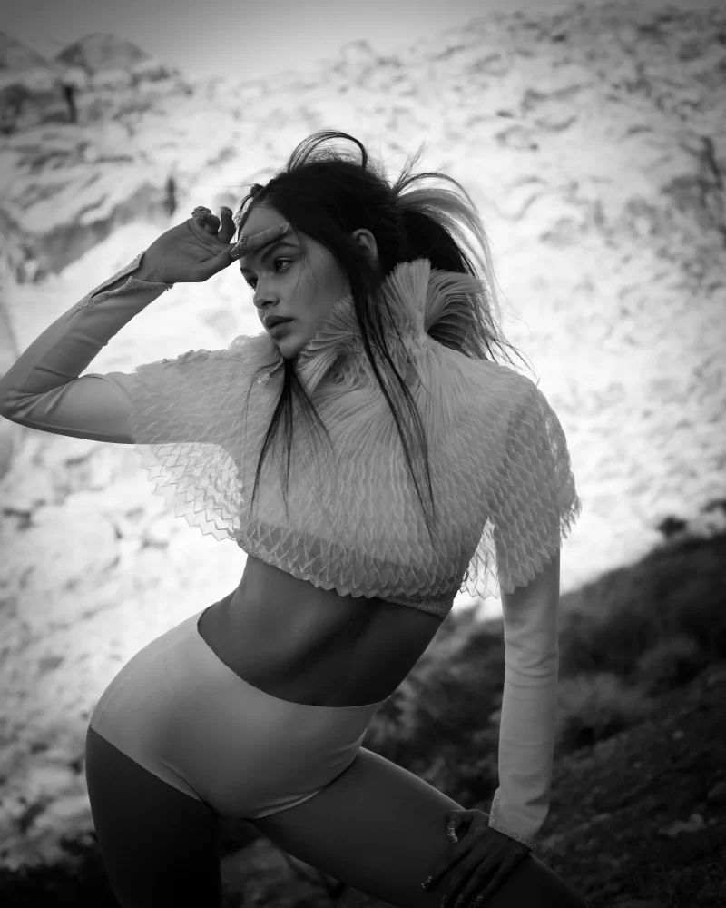Modelo de perfil con peinado alto y crop top plisado, posando en el desierto en fotografía blanco y negro.