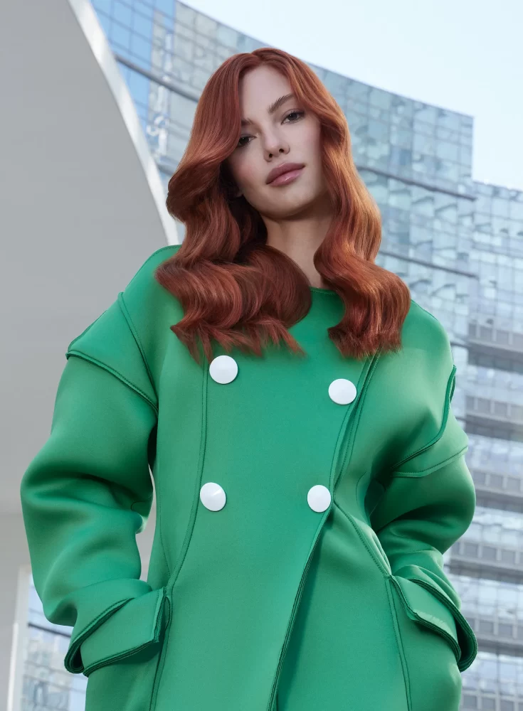 Modelo con corte bob cobrizo brillante, maquillaje editorial y fondo urbano con texturas geométricas en tonos blancos y grises.