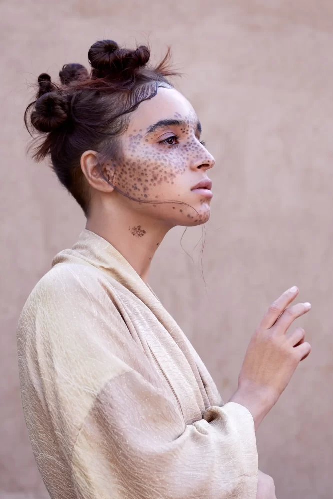 Modelo de perfil con moños en nudos, maquillaje puntual y bata kimono en tonos crema de la colección Divine Feminine de Juliette Den Ouden.