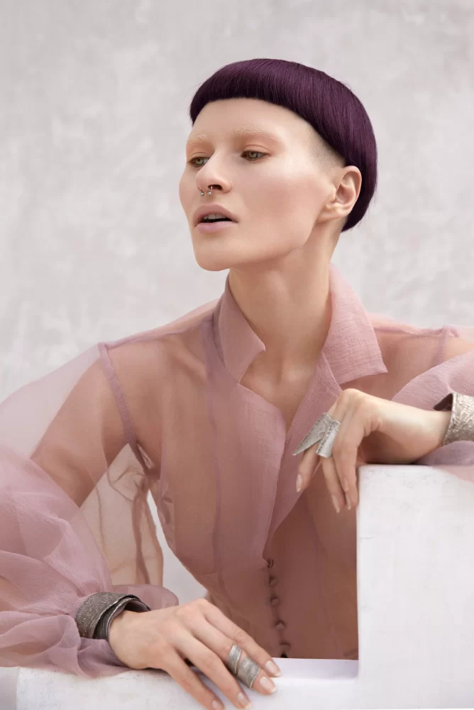 Primer plano de modelo con bordes afeitados, cabello púrpura en corte geométrico y blusa rosa translúcida de Divine Feminine por Juliette Den Ouden.
