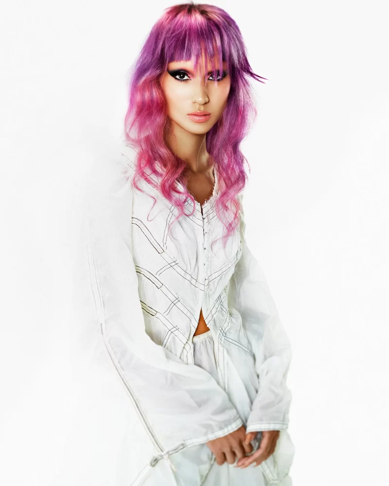 Modelo con cabello fantasía en tonos rosa y violeta, peinado ondulado y fleco irregular, look editorial de la colección Skittles de George Alderete.