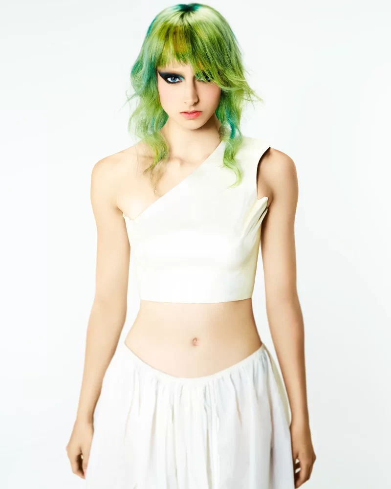 Modelo con cabello teñido en verde neón y toques azul pastel, fleco recto y ondas suaves, estilo editorial futurista de Skittles por George Alderete.