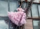Modelo con cabello azul, vestido rosa de tul en capas y escalinata metálica de fondo.