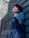 Modelo con cabello corto en tono borgoña y vestido azul, apoyada en una barda metálica con alambre.