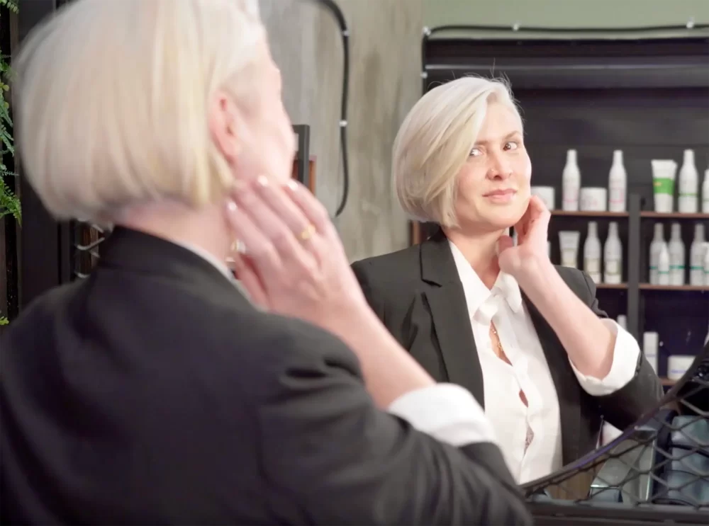 Modelo con corte bob platinado se observa al espejo, mostrando el resultado de la colección We Love You para Yellow Professional.