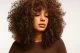 Mujer con cabello rizado voluminoso en tonos castaños cálidos, estilo natural de la colección Igora Zero de Schwarzkopf Professional.