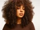 Mujer con cabello rizado voluminoso en tonos castaños cálidos, estilo natural de la colección Igora Zero de Schwarzkopf Professional.