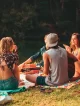 Grupo de amigos en picnic junto al lago disfrutando de una tarde al aire libre con guitarra y sonrisas