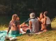 Grupo de amigos en picnic junto al lago disfrutando de una tarde al aire libre con guitarra y sonrisas