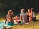 Grupo de amigos en picnic junto al lago disfrutando de una tarde al aire libre con guitarra y sonrisas