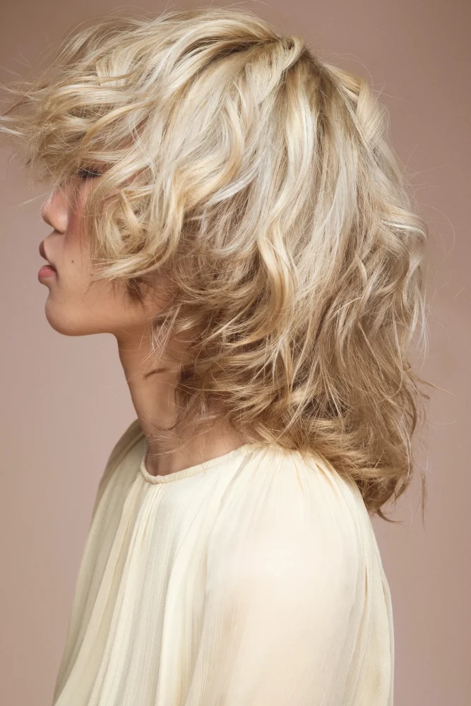 Perfil lateral de modelo femenina con cabello rubio texturizado y capas suaves de Schwarzkopf Professional.